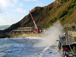 Waves spray up on the beach as a crane works on the beach huts in Torquay