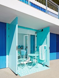 Doors open to a turquoise painted beach hut with matching chairs, table and towels.