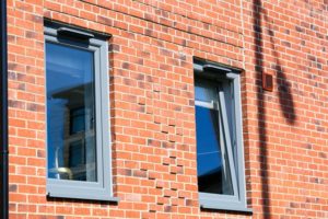 Two 7155 silver grey-foiled uPVC tilt and turn windows in red brick facade by Liniar 