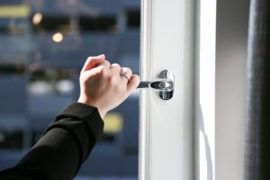 Woman's hand turning a silver handle of a Liniar uPVC white tilt and turn window