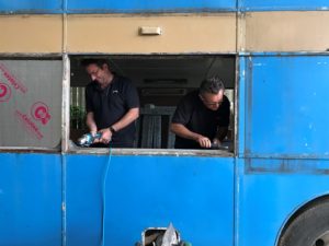 Two men working to cut out windows on the side of the bus during the transformation